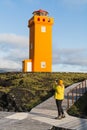 SNAEFELLSNES,Woman in yellow raincoat taking picture of Svortuloft Lighthouse, Snaefellsnes peninsula, Iceland
