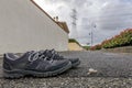 A snail crawls on the asphalt near a pair of sneakers with a high voltage pylon in the background and the cloudy sky Royalty Free Stock Photo