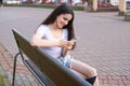 A cute girl is sitting on a bench and writing a message on the phone to a guy