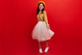 Snapshot full-length of curly dark-haired girl in bright outfit. Woman in beret and fluffy skirt is spinning on red