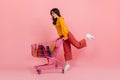 Snapshot full-length if girl shopaholic in bright outfit. Model carries supermarket trolley with packages.