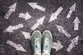 Sneaker shoes and arrows pointing in different directions on asphalt, choice concept Royalty Free Stock Photo