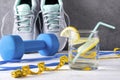 Sneakers, blue dumbbell, glass of water with lemon, measuring tape, jump rope, on a gray