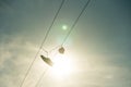 Sneakers hang on electric line wire cable with sun and sky on background. Funny urban outdoor footwear pair silhouette Royalty Free Stock Photo
