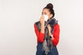 Sneeze and cough, flu symptoms. Portrait of unhealthy young woman wrapped in warm scarf cleaning nose with napkin Royalty Free Stock Photo