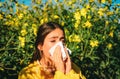 Sneezing young girl with nose wiper among blooming flowers in park. Young woman got nose allergy, flu sneezing nose. The