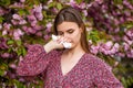 Sneezing young girl with nose wiper among blooming trees in park. Pollen allergy, girl sneezing. Allergy, sneezing Royalty Free Stock Photo