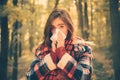 Sneezing young girl with nose wiper among yellow trees in park. Healthcare. Young woman blowing nose at nature. Female