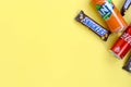 Snickers chocolate bar in brown wrapping lies with red Coca Cola and orange Fanta tin can on yellow pastel background. Famous