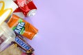 Snickers chocolate bar wrapping lies with empty red Coca Cola and orange Fanta tin cans next to mcdonalds paper bags and cups on