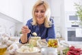 Sniling blond woman picks a teaspoon of crushed garlic from a jar in the kitchen Royalty Free Stock Photo