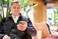 Sniling male in leather jacket with smartphone while sitting on chair in store against green plant Royalty Free Stock Photo