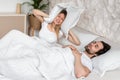 Snoring young guy and his frustrated girlfriend covering ears with pillow in bed at home Royalty Free Stock Photo