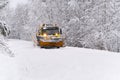 A snow blower car clears snow in the forest from the road on a winter morning. Snow plow truck cleaning icy white road Royalty Free Stock Photo