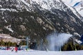 Snow canons blowing fresh snow on ski slope. Skiers on slopes with chairlifts and Pyrenees mountains in background.