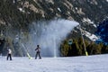 Snow canons blowing fresh snow on ski slope. Skiers on slopes with chairlifts and Pyrenees mountains in background