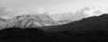 Snow-capped mountains with dark dry, barren mountains in the foreground under a cloudy sky in California Royalty Free Stock Photo