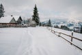 Snow-capped wooden fence, houses in mountains Carpathians Ukraine. On background Christmas tree in forest. Winter nature.