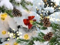 Snow Christmas tree branch and pine  cones  with garland blurred  festive light and red folium bow in winter forest Royalty Free Stock Photo