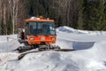 Snow-cleaning bulldozer, for cleaning the ski slope, standing in a snowdrift, against the backdrop of the forest in sunny weather Royalty Free Stock Photo