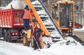 Snow cleaning tractor snow-removal machine loading pile of snow on a dump truck. Snow plow outdoors cleaning street city