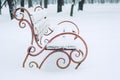 Snow-covered bench with heart symbol in the city park. Forged metal and wooden park bench and trees covered by heavy snow. Winter Royalty Free Stock Photo