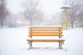 snow-covered bench in misty morning
