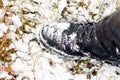 Snow-covered black boot of a man on his feet while walking in a winter park, top view. Man in black boots in the snow Royalty Free Stock Photo