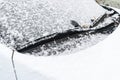 Snow covered car window with wipers, macro, close up. Car wiper blades clean snow from car windows. Flakes of snow covered the car