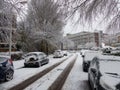 Snow covered cars parked on snowy tree lined suburban urban city street during snow storms in Europe