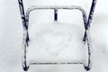 Snow-covered children`s swings. On the seat in the snow figure in the shape of heart.