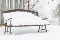 Snow covered empty vintage old garden bench on a col wet misty snowy day