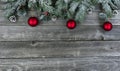 Snow covered evergreen branches plus bright red ornaments on faded wooden planks for a merry Christmas or happy New Year holiday Royalty Free Stock Photo