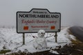 Snow covered fells at the Northumberland / Cumbria border sign with a frightening looking snowman in the foreground Royalty Free Stock Photo