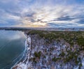 Snow-covered forest on lake shore with the first ice at sunset and the city on horizon, auerial view Royalty Free Stock Photo