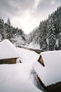 Snow covered and frozen wooden cabins in the middle of mountain forest with stream on background in winter. Snowy slovak