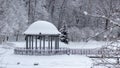 Snow-covered gazebo with a metal bridge in the middle of a lake in the park Royalty Free Stock Photo