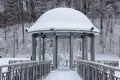 Snow-covered gazebo with a metal bridge in the middle of a lake in the park Royalty Free Stock Photo