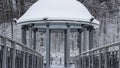 Snow-covered gazebo with a metal bridge in the middle of a lake in the park Royalty Free Stock Photo