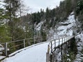 Snow-covered iron pedestrian bridge over the canyon of the Fallbach alpine stream at the foot of the Alpstein mountain range Royalty Free Stock Photo