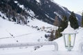 Snow covered lantern between two railings with Tyrol Alps ski resort on background.