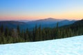 From the snow covered lawn opens a view of green fir trees, high mountains with snow covered tops, sunset, blue sky. Royalty Free Stock Photo