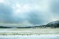 Snow covered meadow with village, mountains and ominous sky