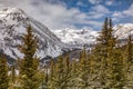 Snow covered mountain peaks and green pine trees under partly cloudy skies Royalty Free Stock Photo