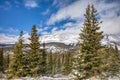 Snow covered mountain peaks and green pine trees under partly cloudy skies Royalty Free Stock Photo