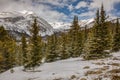 Snow covered mountain peaks and green pine trees under partly cloudy skies Royalty Free Stock Photo