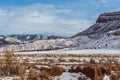 Snow covered mountain range behind red rock field with brush in rural New Mexico