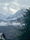 Snow-covered mountains with mist and trees in the foreground. A serene winter landscape under a cloudy sky Royalty Free Stock Photo