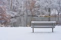 A snow-covered park bench overlooking a pond Royalty Free Stock Photo