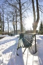 Snow-covered park with melted footpath. Beautiful winter landscape in the city. Decorative streetlamps and park benches in a row